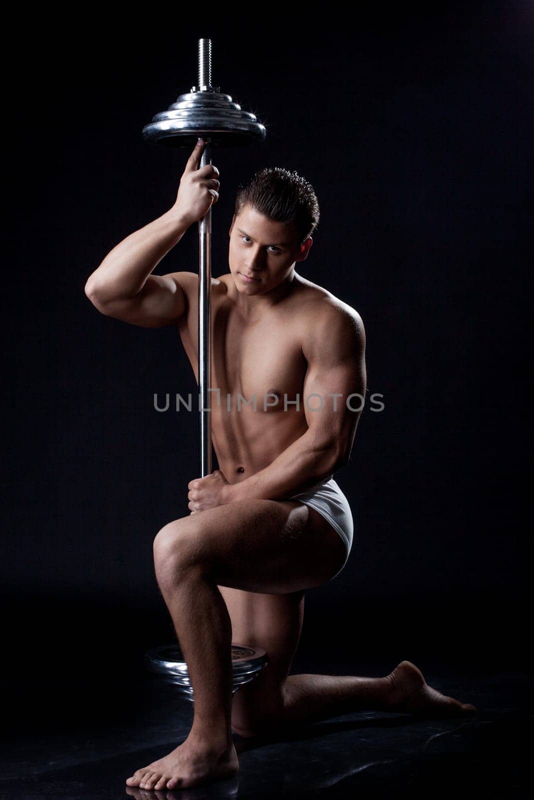 Muscular young athlete posing looking at camera, isolated on black