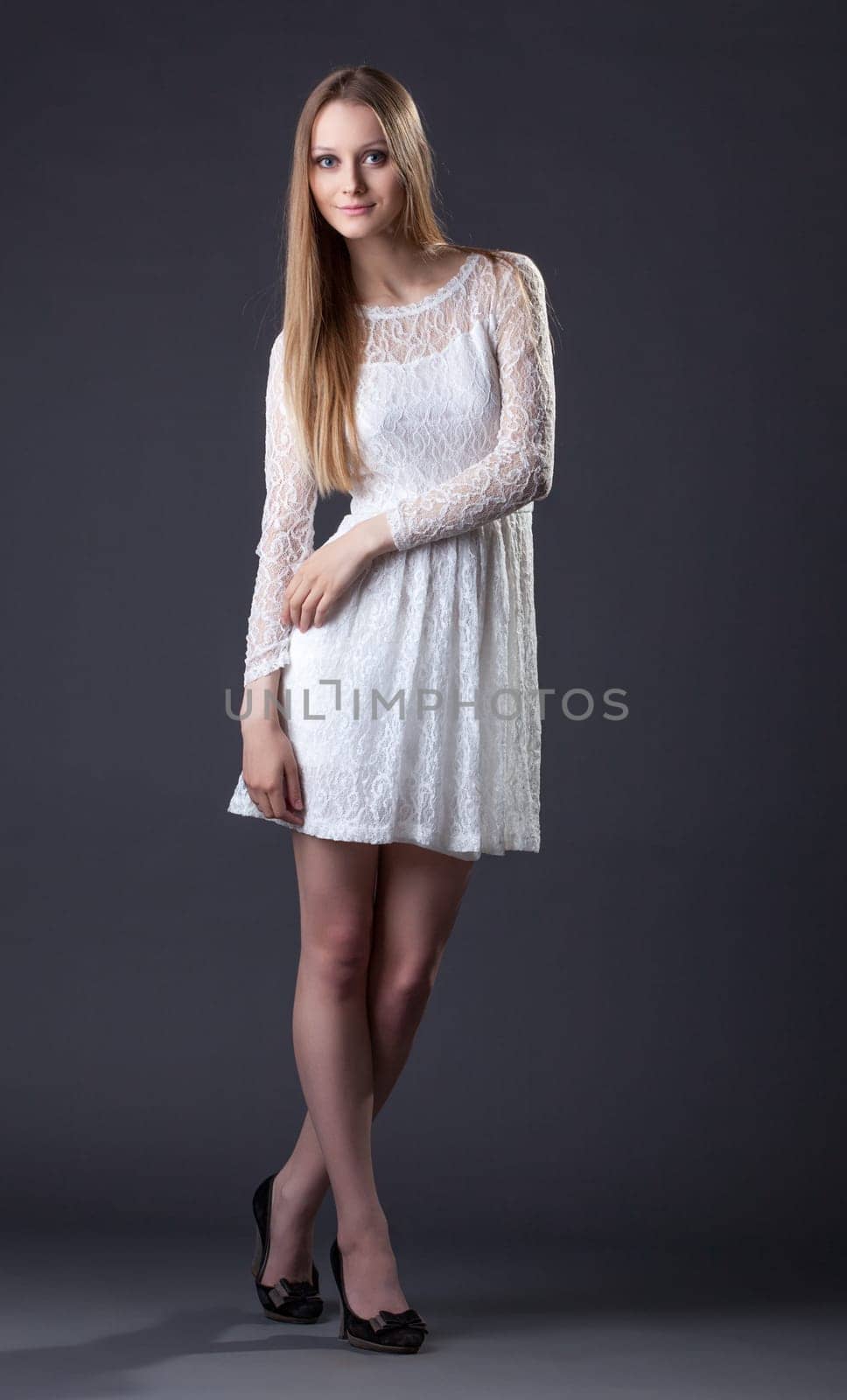 Beautiful tall model posing in white lace dress, on gray background