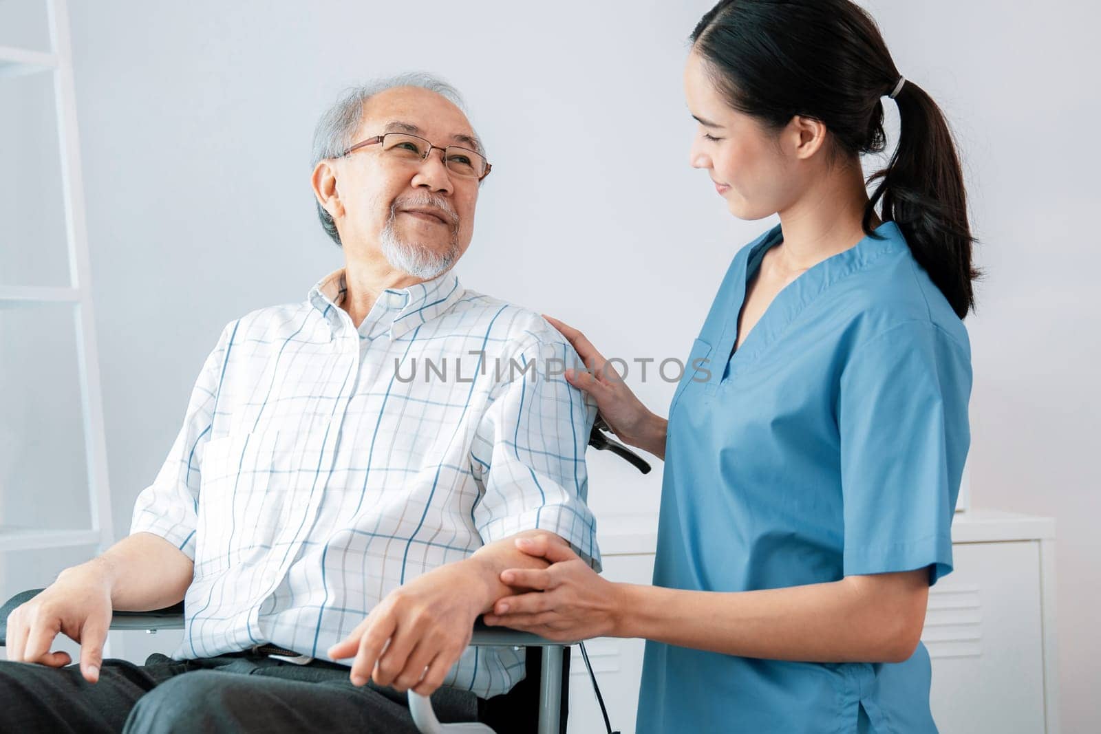 Happy positive asian nurse giving support and touching contented senior man with love. Nursing home for the elderly, elderly health and illness, senior patient carer.