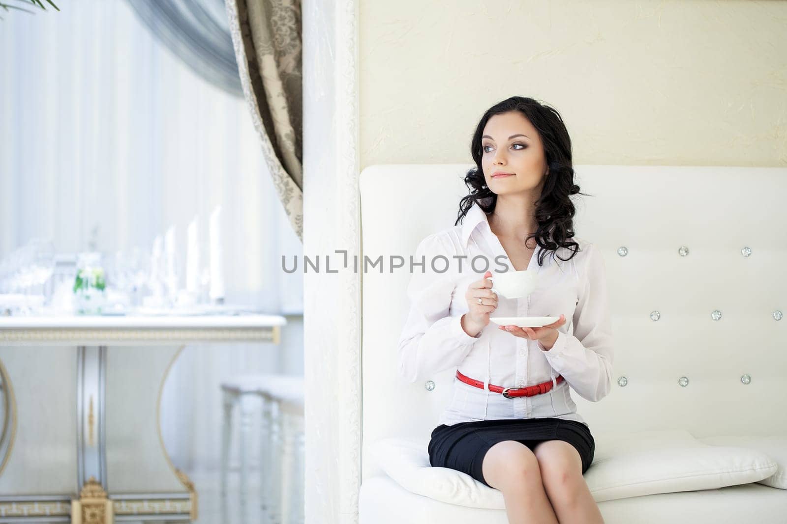 Image of young curly brunette drinking coffee in hotel room