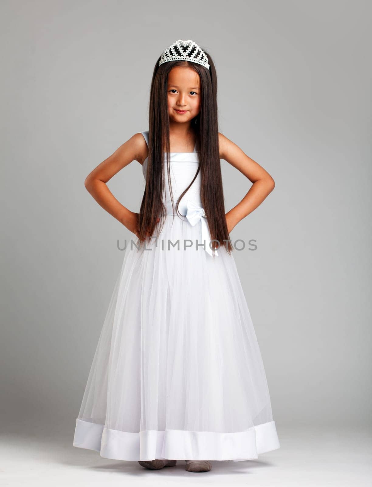 Cute little brunette in elegant dress and crown, on gray background