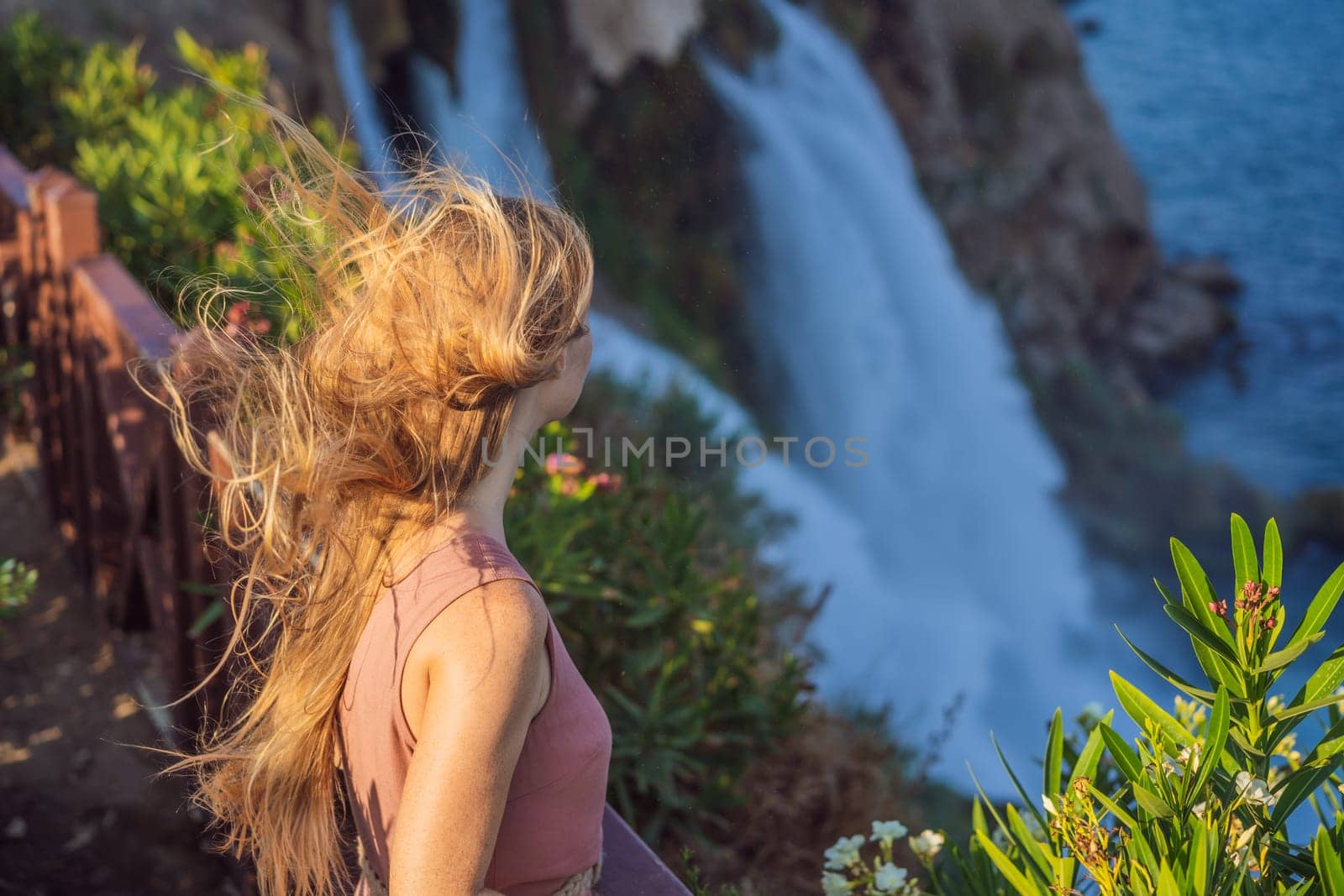 Beautiful woman with long hair on the background of Duden waterfall in Antalya. Famous places of Turkey. Lower Duden Falls drop off a rocky cliff falling from about 40 m into the Mediterranean Sea in amazing water clouds. Tourism and travel destination photo in Antalya, Turkey. Turkiye.