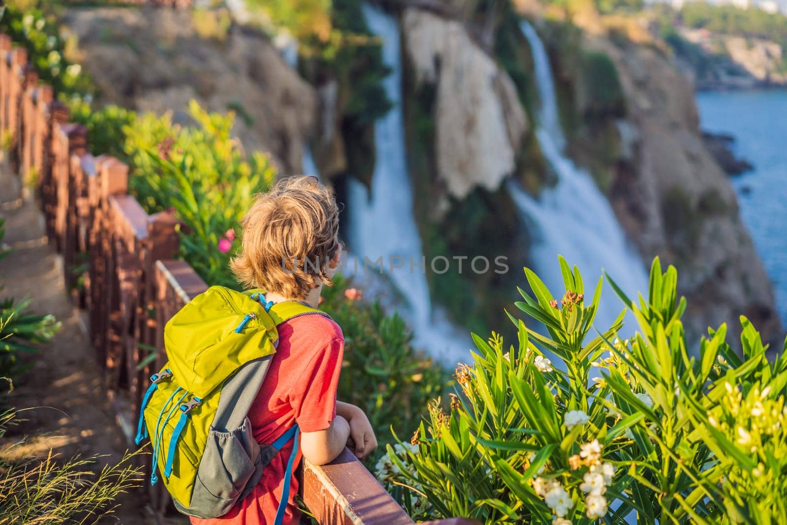 Boy tourist with a backpack on the background of Duden waterfall in Antalya. Famous places of Turkey. Lower Duden Falls drop off a rocky cliff falling from about 40 m into the Mediterranean Sea in amazing water clouds. Tourism and travel destination photo in Antalya, Turkey. Turkiye.