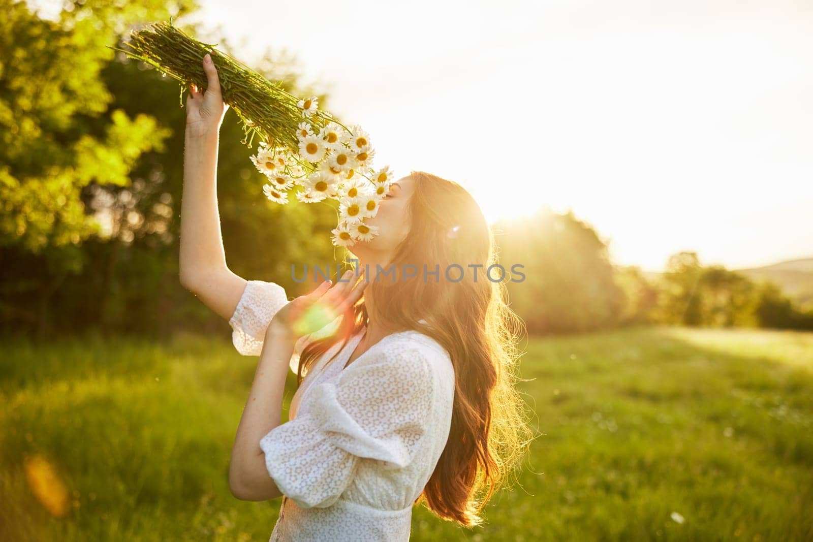 close portrait of a red-haired woman in a light dress sniffing a bouquet of daisies. nature, sunny weather. High quality photo