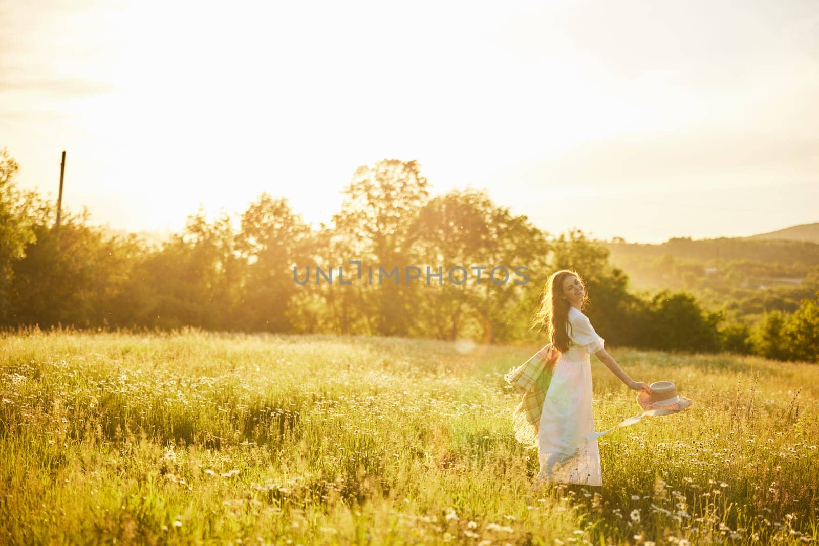 a woman in a light dress with a hat in her hands is spinning in nature in the rays of the setting sun. High quality photo