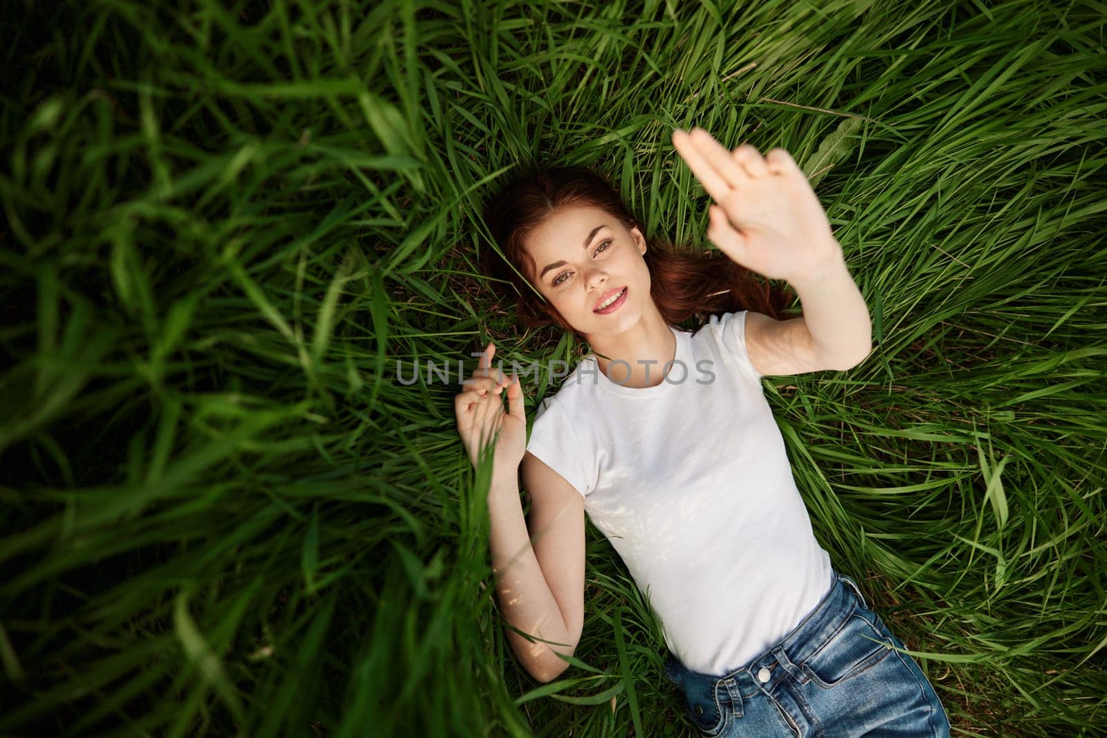 attractive teenager lying down on green grass with hands rised up to the air. High quality photo