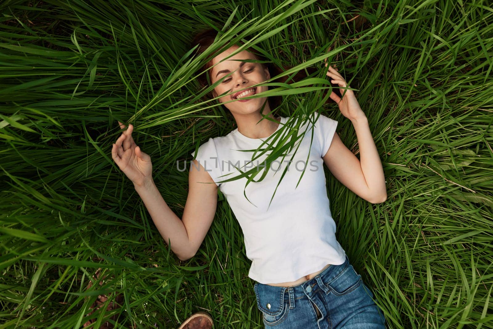 happy woman lies in high grass biting leaves with beautiful, even teeth. High quality photo