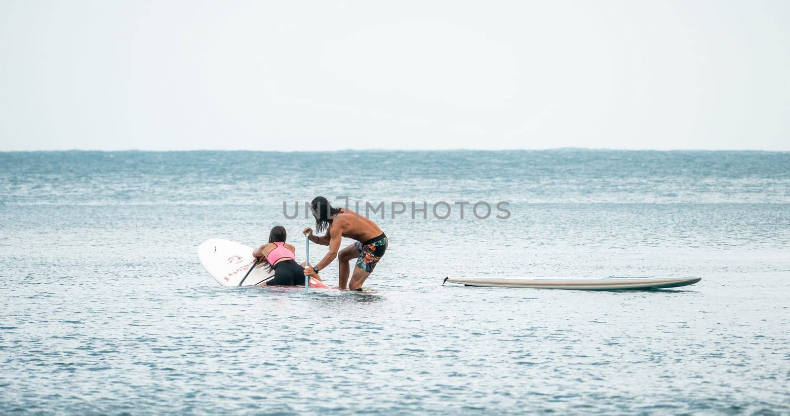 Sea woman and man on sup. Silhouette of happy young woman and man, surfing on SUP board, confident paddling through water surface. Idyllic sunset. Active lifestyle at sea or river