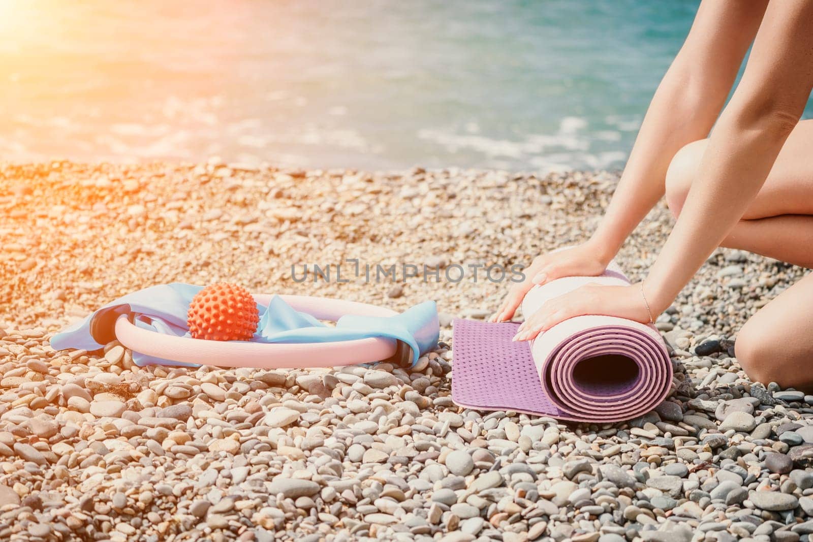 Young woman with long hair in white swimsuit and boho style braclets practicing outdoors on yoga mat by the sea on a sunset. Women's yoga fitness routine. Healthy lifestyle, harmony and meditation