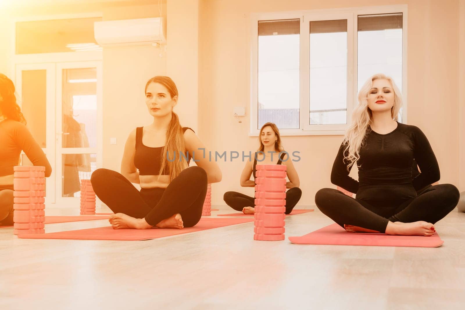 Middle aged well looking women, performing fascia exercises on the floor using a massage foam roller - tool to relieve tension in the back and relieve muscle pain. Female fitness yoga routine concept by panophotograph