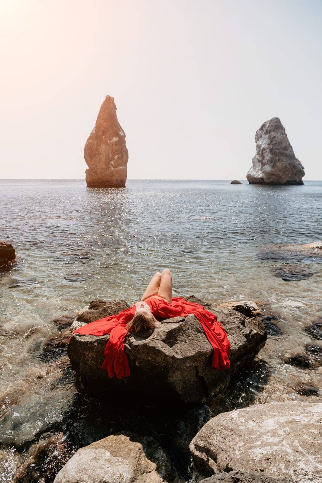 Woman travel sea. Young Happy woman in a long red dress posing on a beach near the sea on background of volcanic rocks, like in Iceland, sharing travel adventure journey