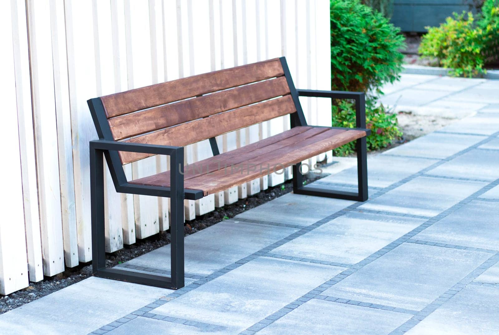 modern bench on the street on a summer day against the backdrop of green bushes. wooden bench in the courtyard of the business center. smoking area. High quality photo
