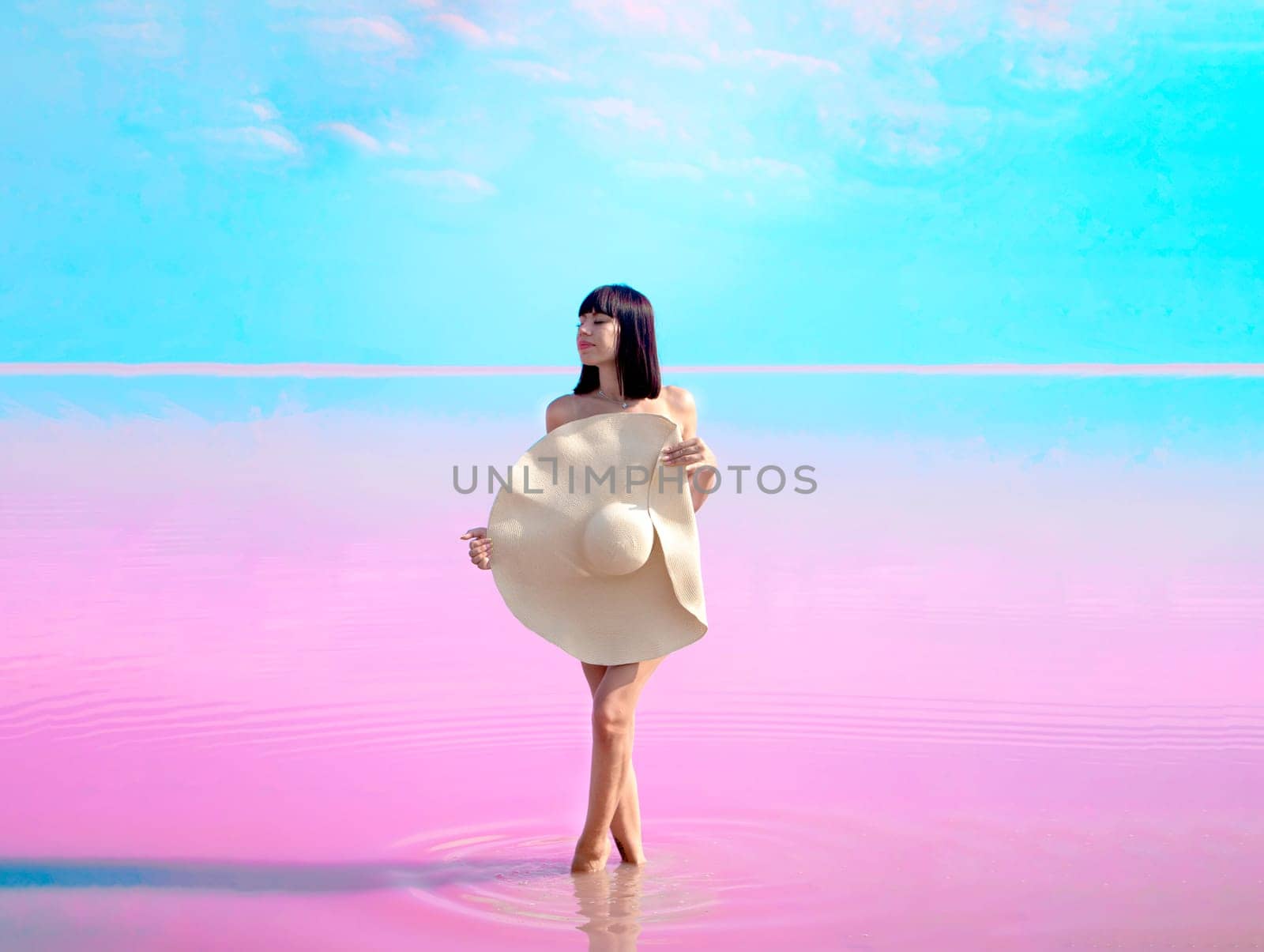 young woman with hat stands against the backdrop of pink lake and blue sky. Tourism in exotic place. Nature miracle. purple water lake. pink blue background. Vacation, travel concept. amazing world.