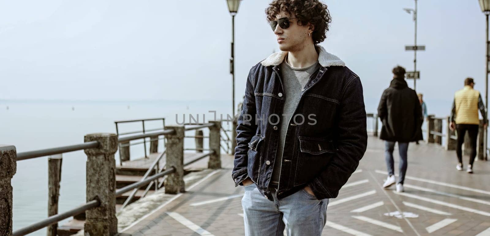 A young man taking a pensive walk along a pier, lost in his thoughts and seemingly carrying a heavy heart.