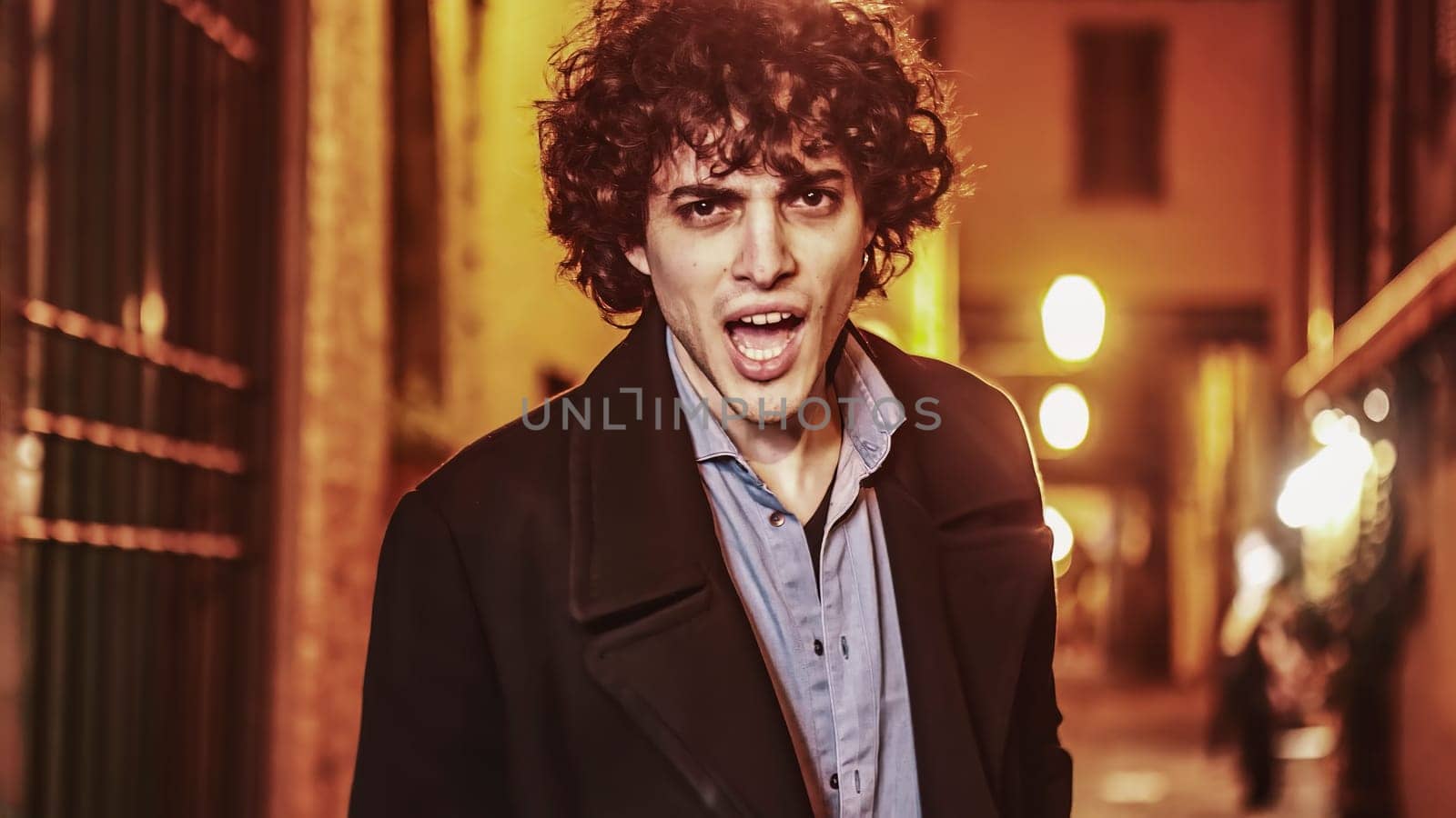 A young man yells out in frustration while standing alone on a dark city street at night.