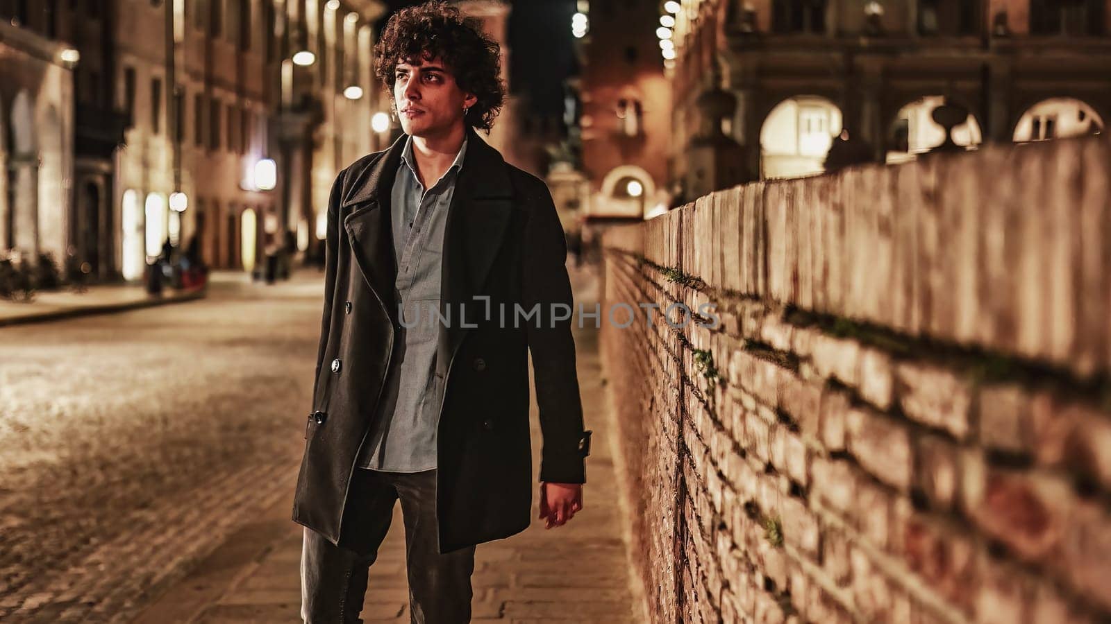 A distressed young man leans against a wall and screams out in a city at night.