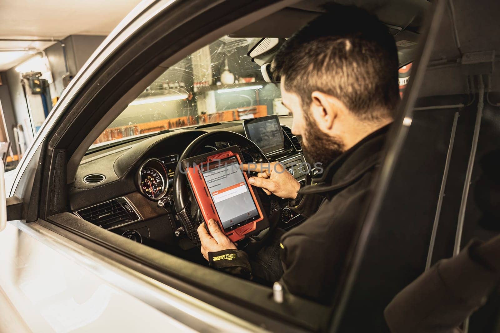 A mechanic's hands use a diagnostic tool to troubleshoot a modern car's computer system in a garage.