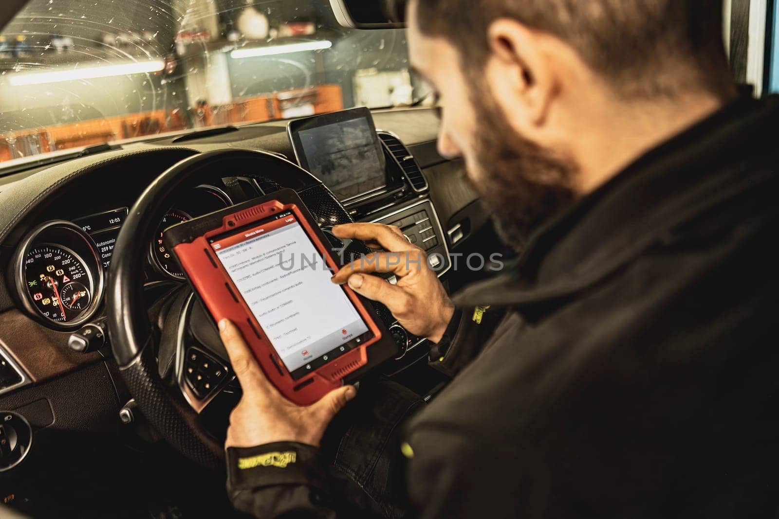 A mechanic's hands use a diagnostic tool to troubleshoot a modern car's computer system in a garage.