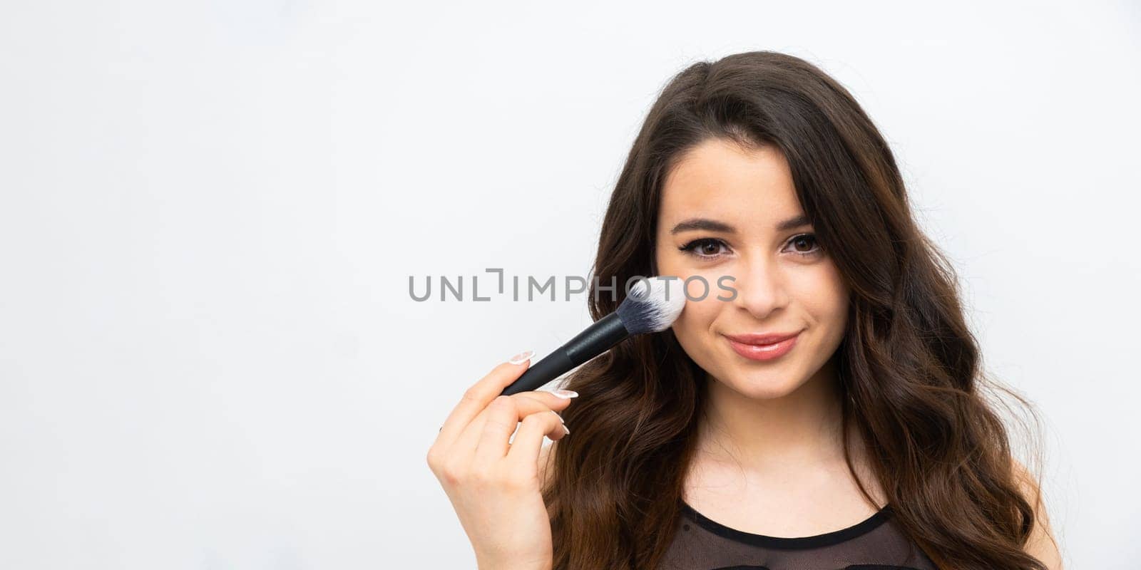 Attractive brunette holding a cosmetic brush near her face on the banner with copy space. Advertising of a beauty salon concept.