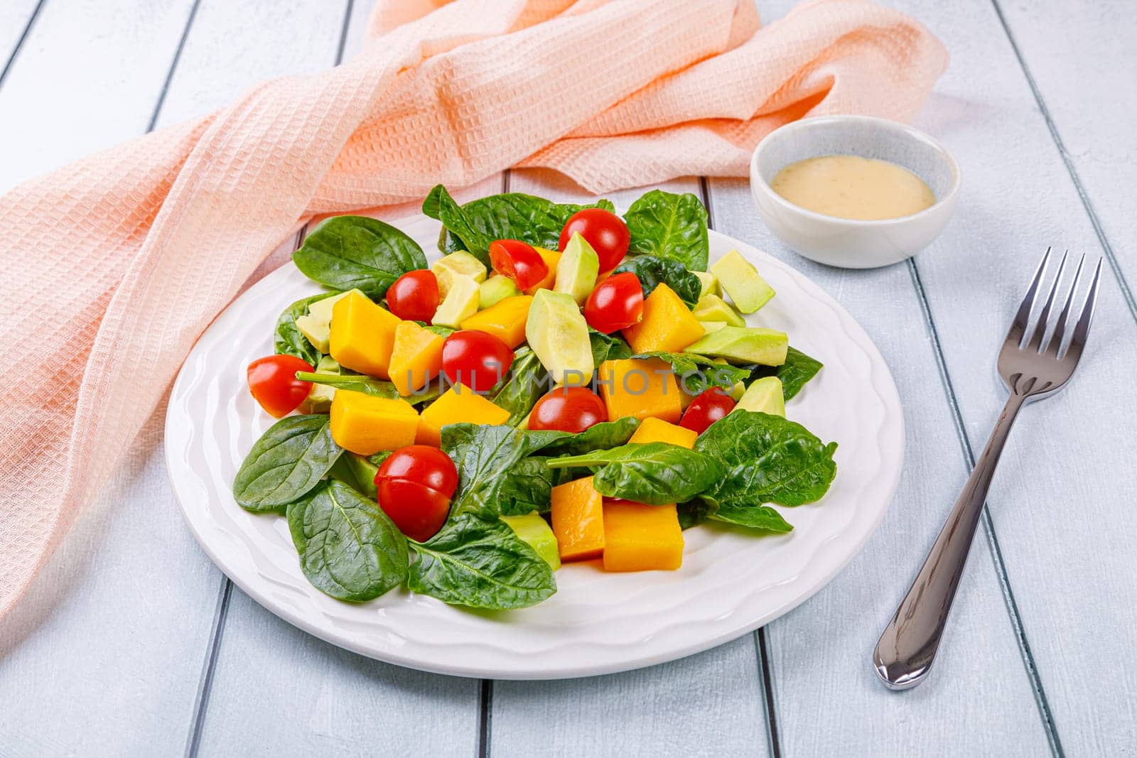 Fresh salad of avocado, mango, spinach and cherry tomatoes in a white plate on a wooden background. High quality photo