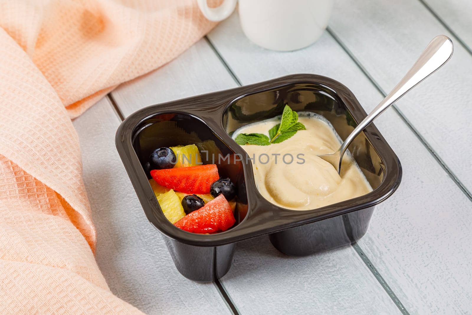 Dessert of applesauce, pineapple and strawberries in a plastic container on a wooden background. High quality photo