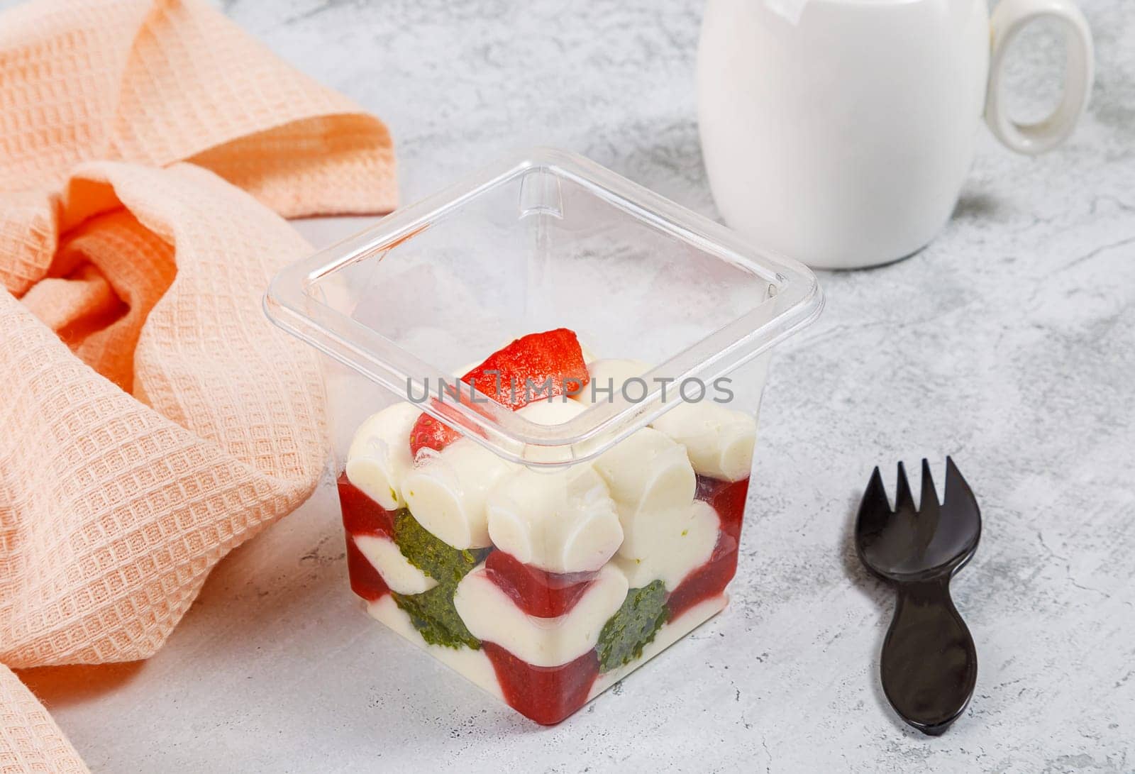 Dessert of cream, spinach, jam and strawberries in a plastic glass on a concrete background. High quality photo