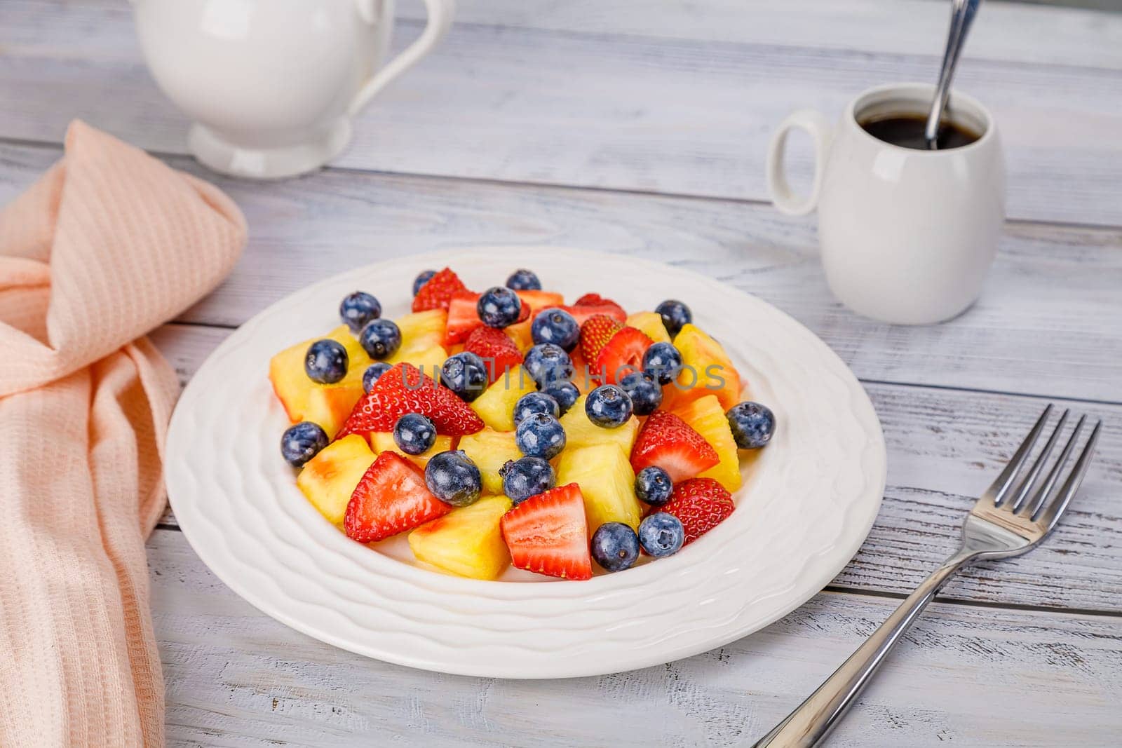 Fruit salad with pineapple, strawberries and blueberries on a white plate. High quality photo