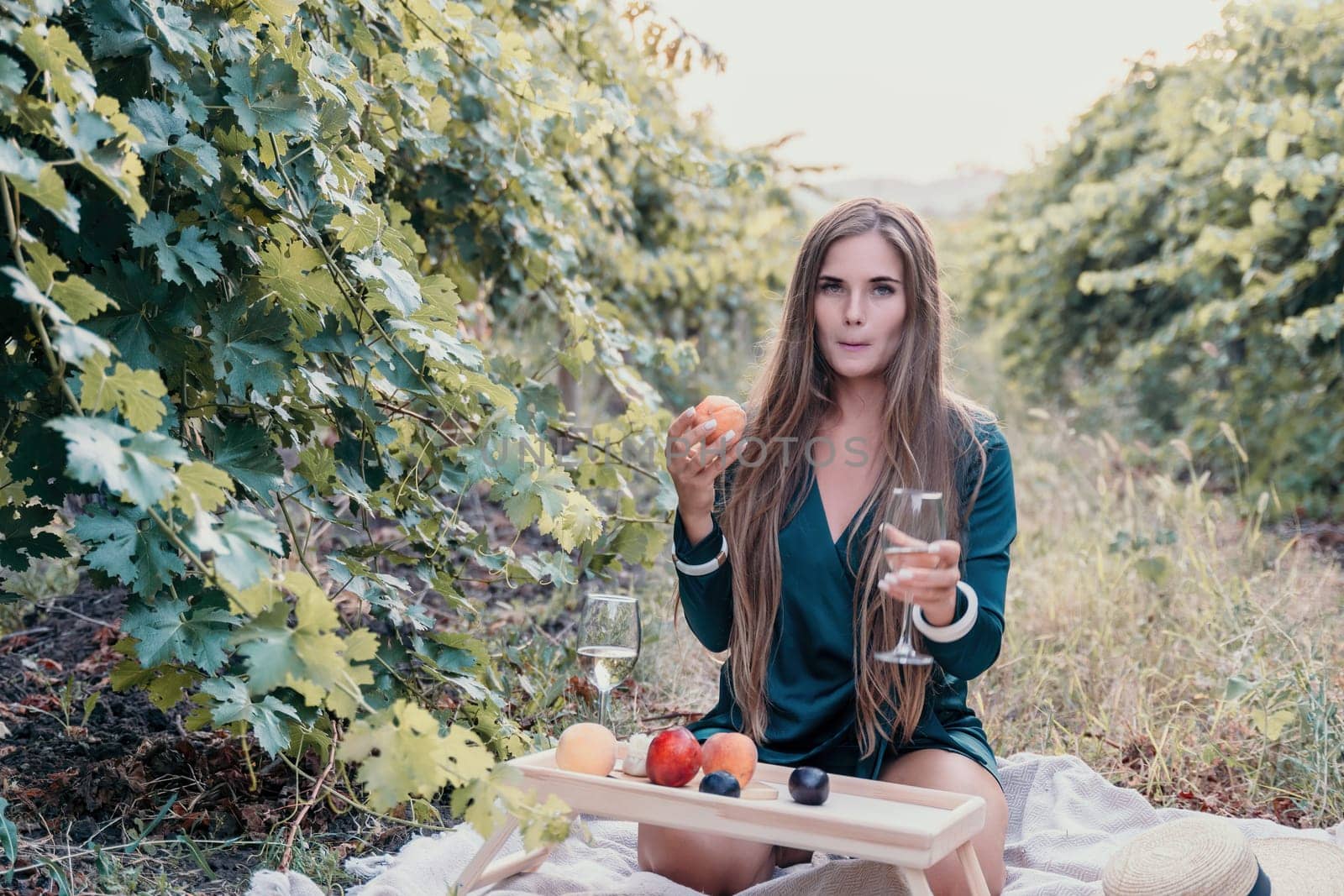 Woman picnic vineyard. Happy woman with a glass of wine at a picnic in the vineyard, wine tasting at sunset and open nature in the summer. Romantic dinner, fruit and wine. by panophotograph
