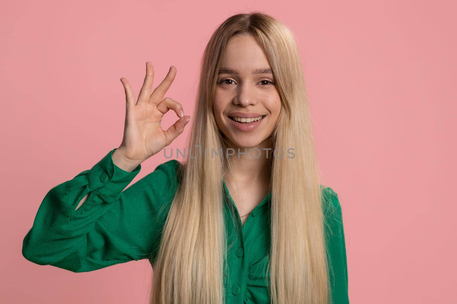 Okay. Joyful happy caucasian woman looking approvingly at camera showing approve feedback gesture like Ok sign positive something good. Pretty smiling girl on pink background. People sincere emotion