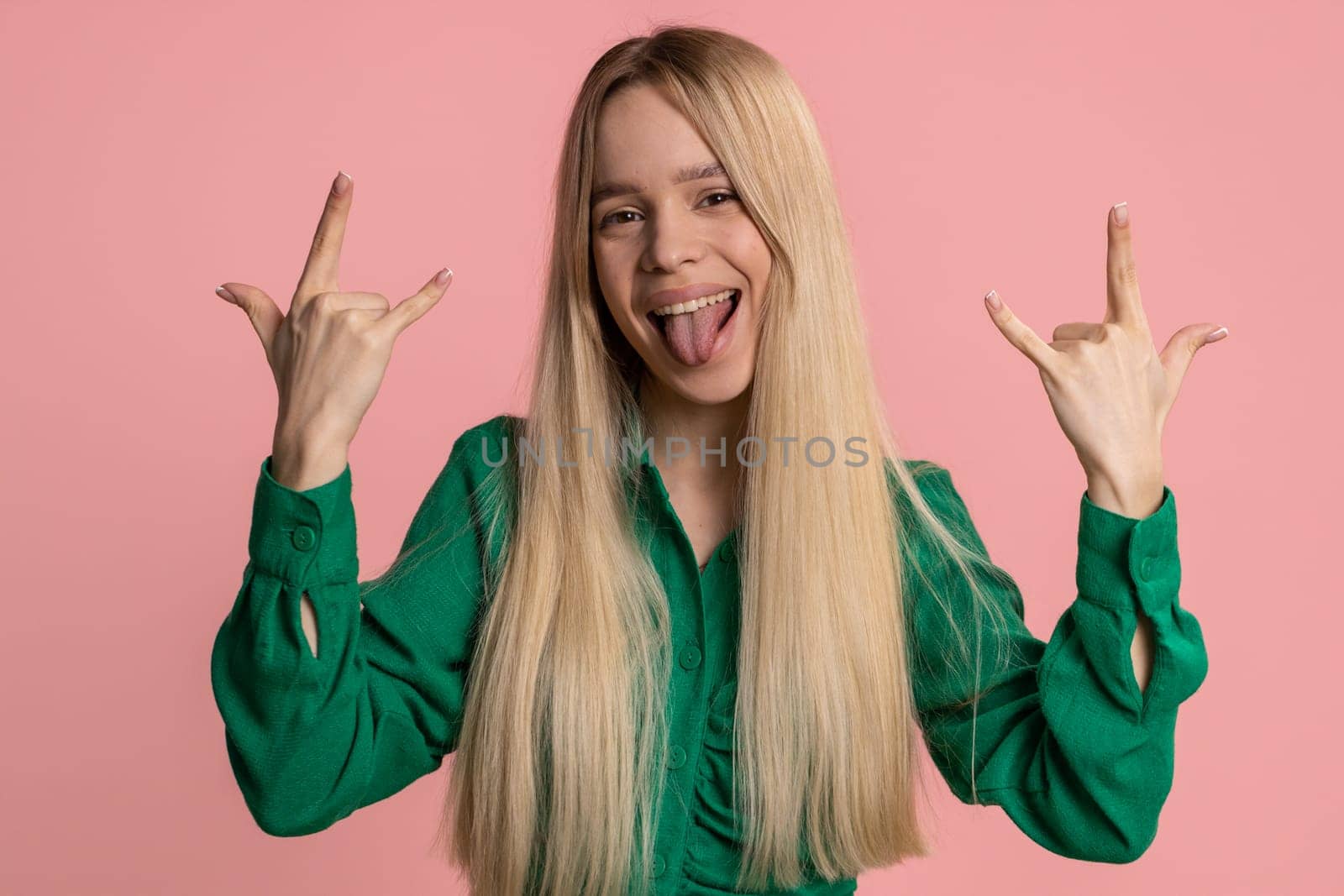 Overjoyed caucasian woman showing rock n roll gesture by hands, cool sign, shouting yeah with crazy expression, dancing, emotionally rejoicing in success. Young happy girl isolated on pink background