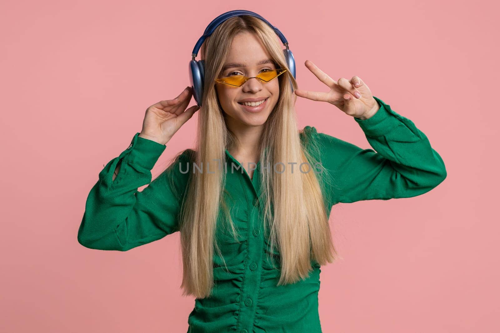 Pretty woman in headphones listening music, smiling dancing disco party, music rhythmically moving her hands, having fun, celebrating success winning, birthday. Teenager girl kid on pink background