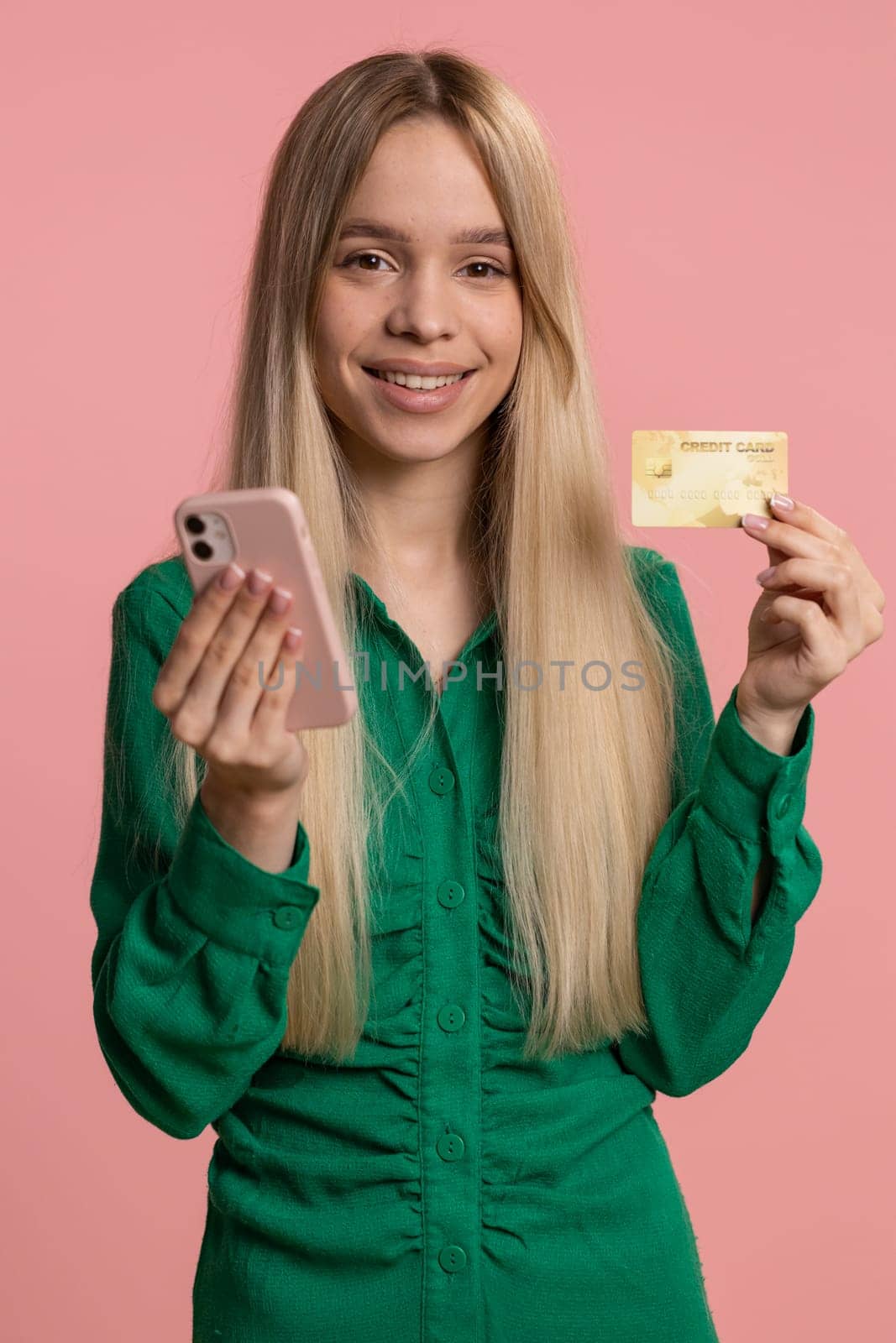 Sincere woman customer using credit bank card and smartphone while transferring money, purchases online shopping, payment. Finance and internet. Happy girl isolated alone on pink background. Vertical