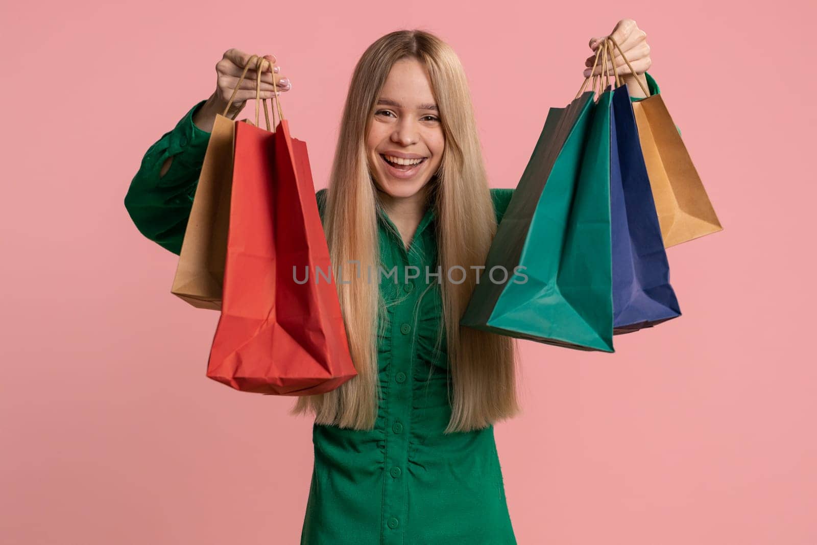 Shopaholic woman showing shopping bags, advertising discounts, smiling looking amazed with low prices, shopping on Black Friday holidays. Child girl celebrate win isolated on pink studio background