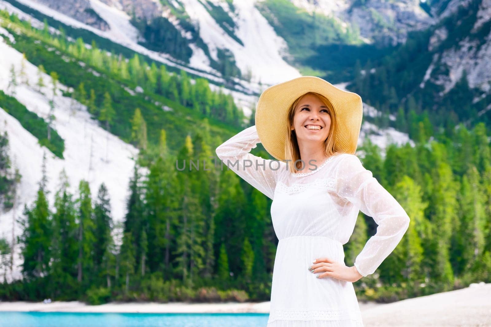 Smiling woman in summer hat and white dress against Dolomites Alps and Braies Lake.