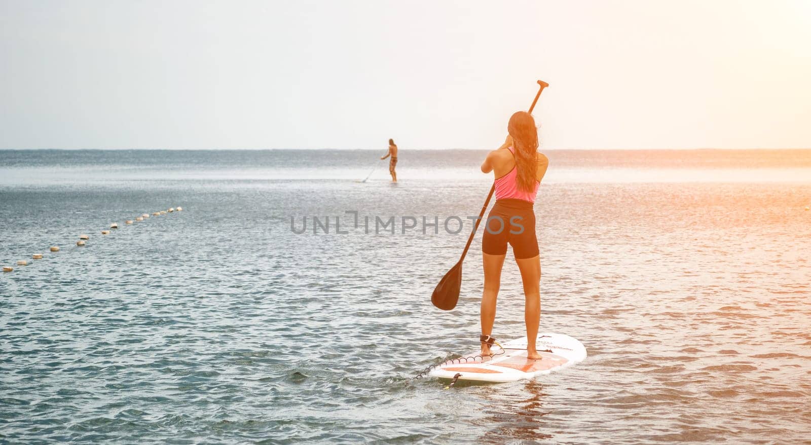 Sea woman and man on sup. Silhouette of happy young woman and man, surfing on SUP board, confident paddling through water surface. Idyllic sunset. Active lifestyle at sea or river