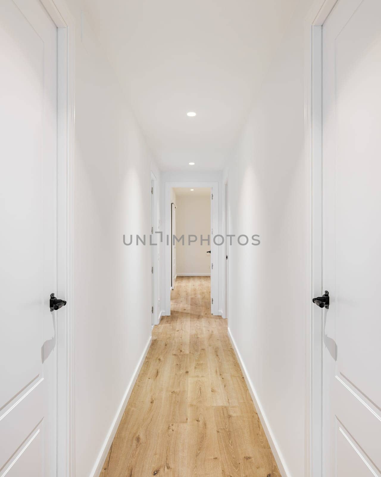 Long narrow straight corridor with doors on the left and right in a mini hotel after renovation. Concept of a cozy hotel and rooms for vacation or business trip. Copyspace.