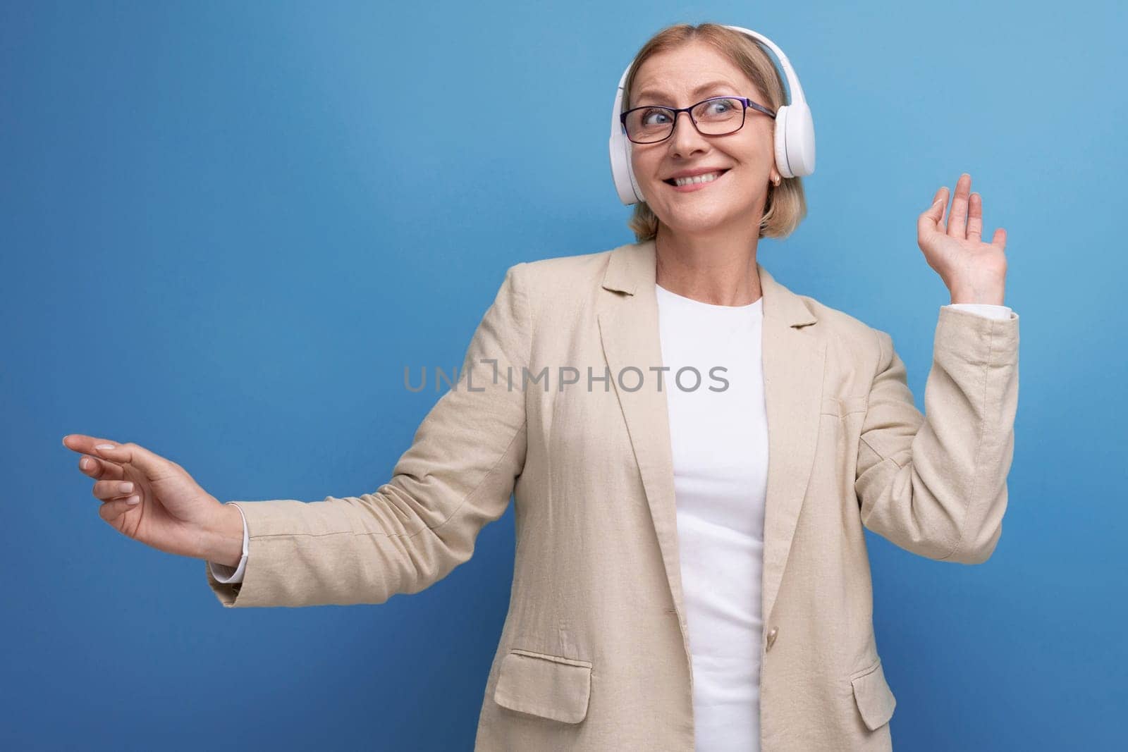 close-up of 50s middle aged woman in jacket enjoying music with headphones on studio background with copy space.