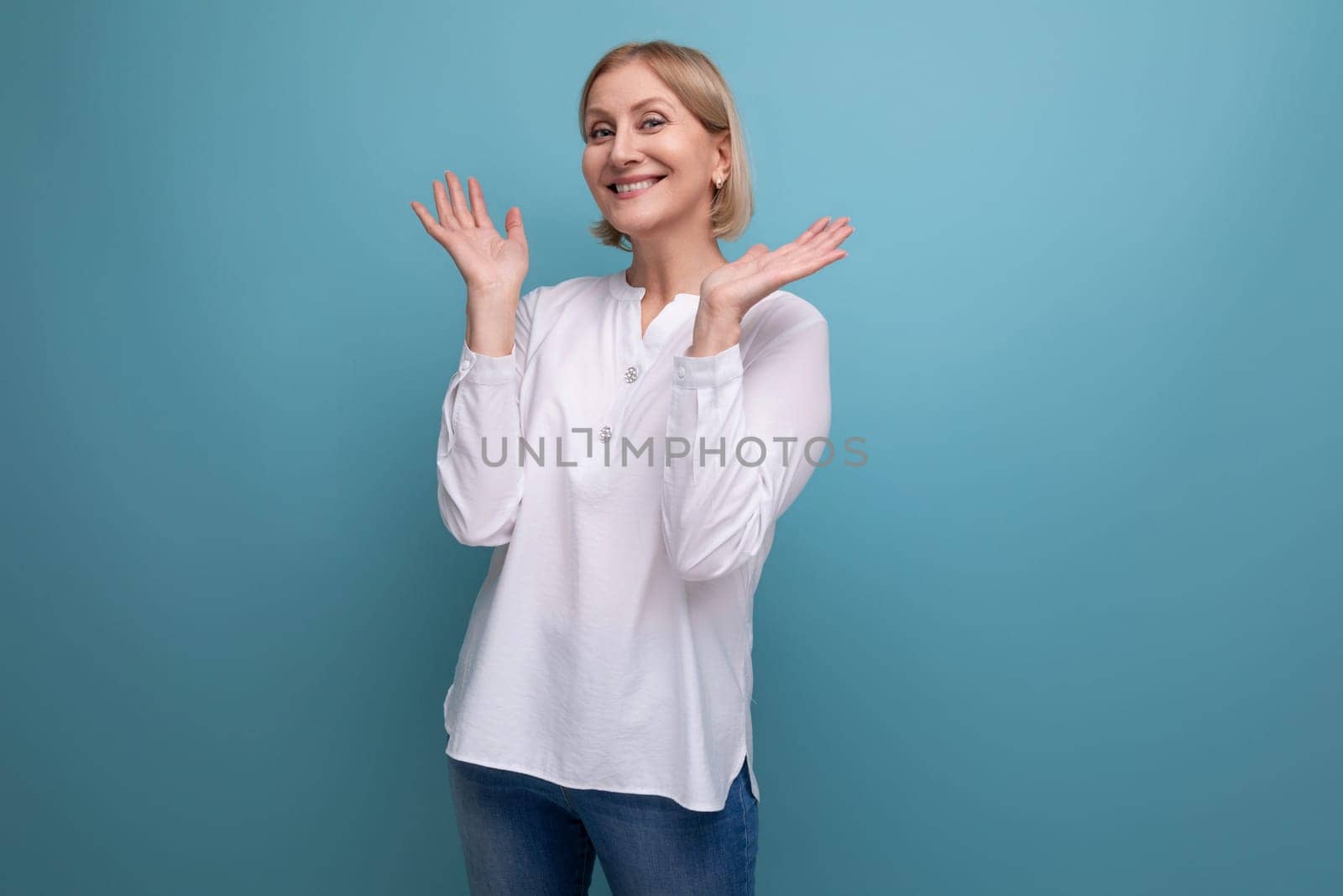cheerful blond 50s woman in white blouse in menopause on studio background.