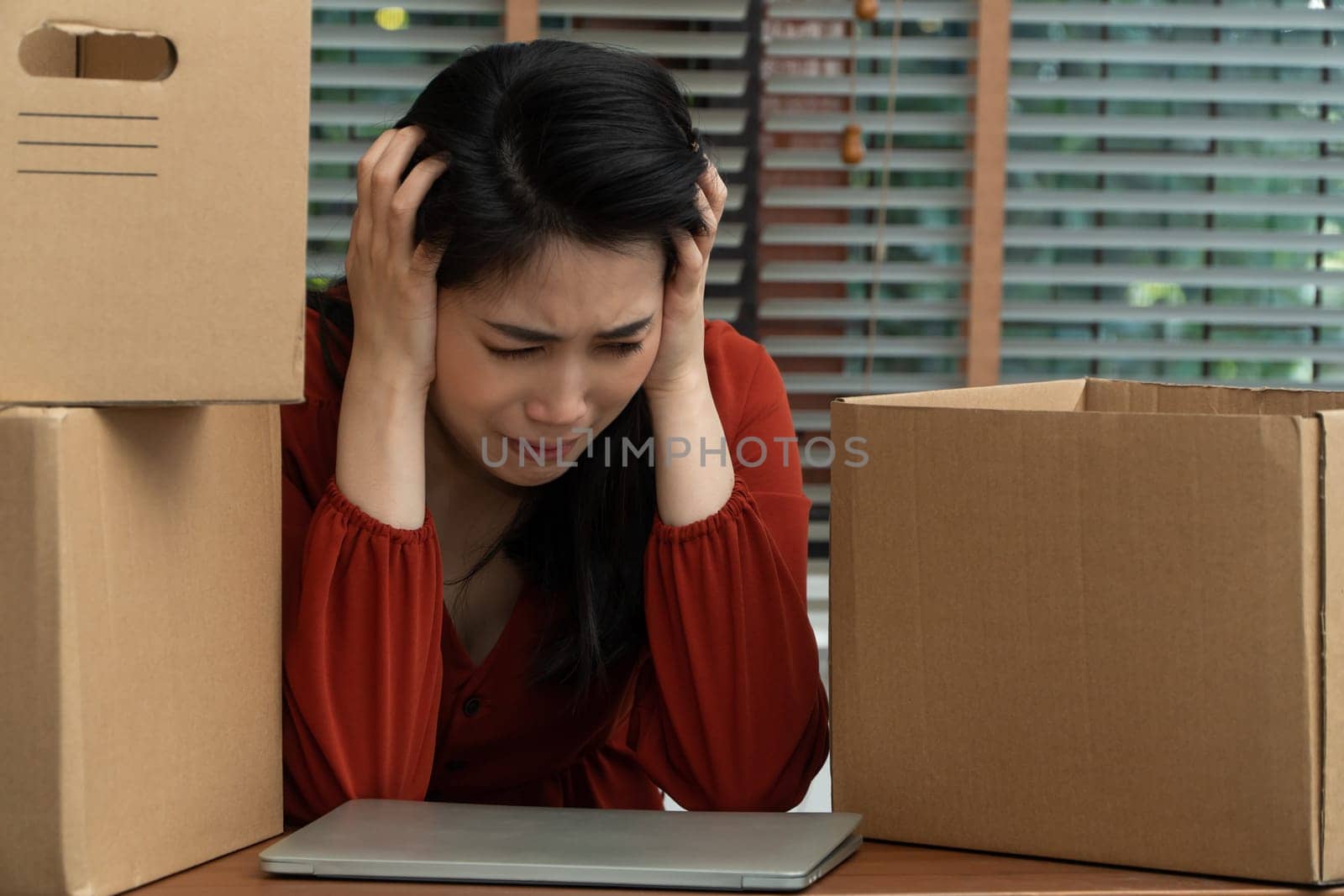 Sad Asian woman Packing belongings in a cardboard box and crying on the desk in the office After being layoff and unemployed. Concept of impact on the economic downturn And management of the failure by PattyPhoto