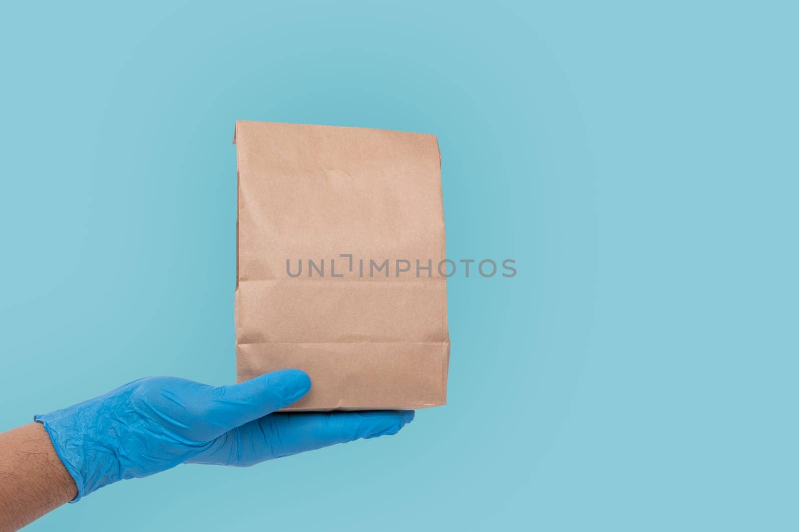Close up hand in medical glove and holding food paper bag on white background ( Isolated background). Concept of Ordering food online and delivery service. by PattyPhoto