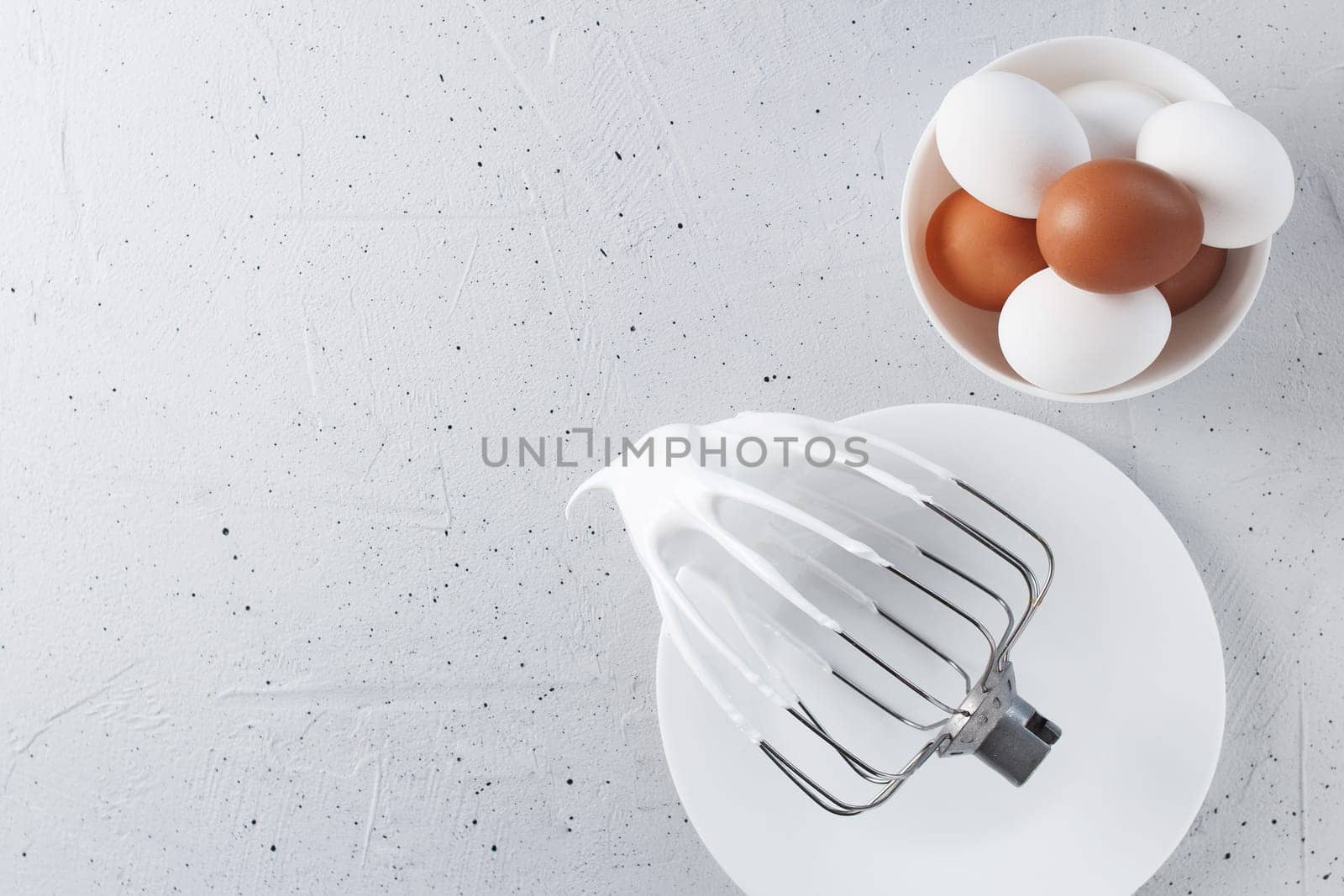 Whisked egg whites - whipped Italian meringue on a wire whisk and eggs on a gray background. copy space. by lara29