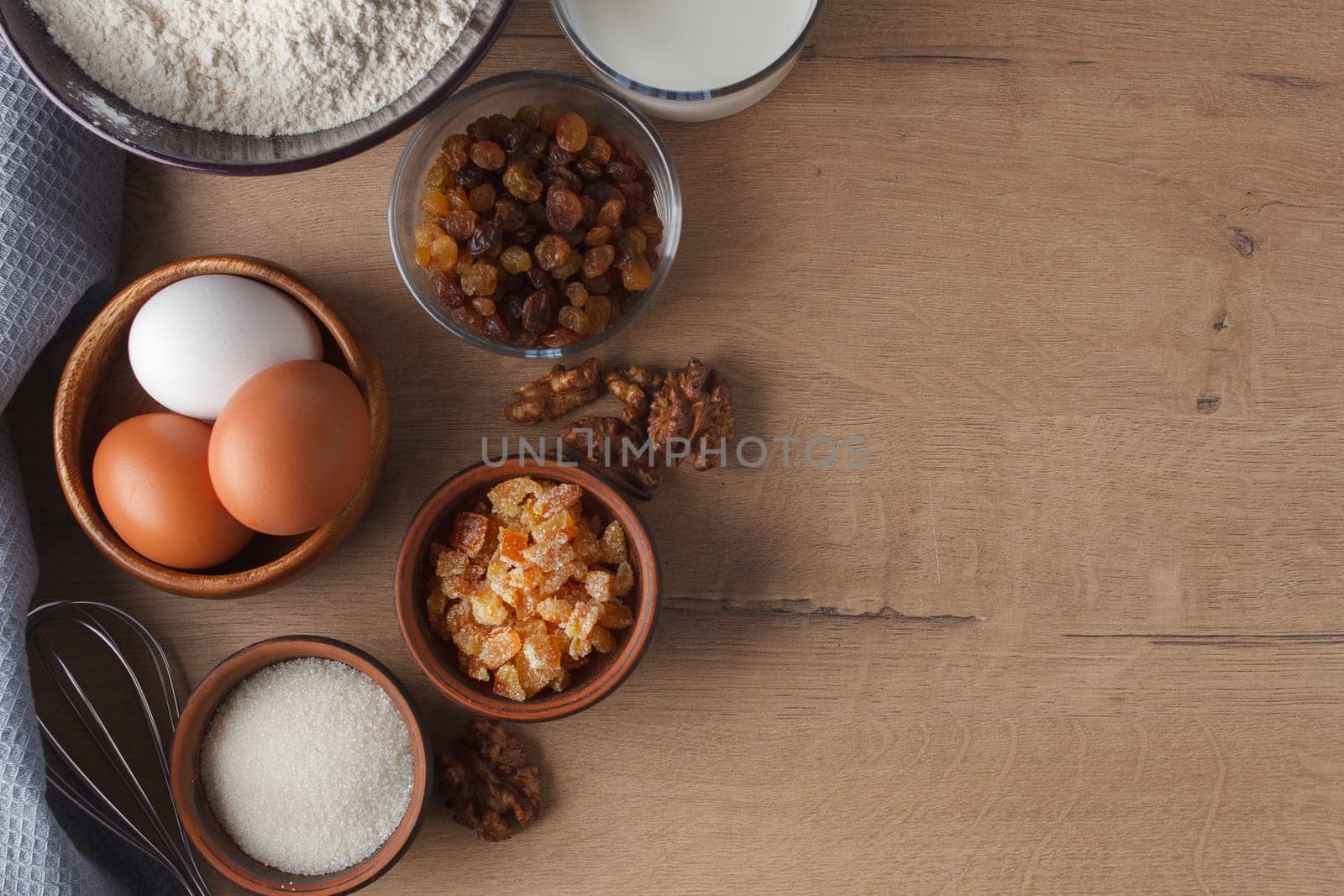 Preparation for cooking sweet pastries. Eggs, sugar, milk, flour, salt, candied fruits, raisins, nuts, whisk on the kitchen table. copy space