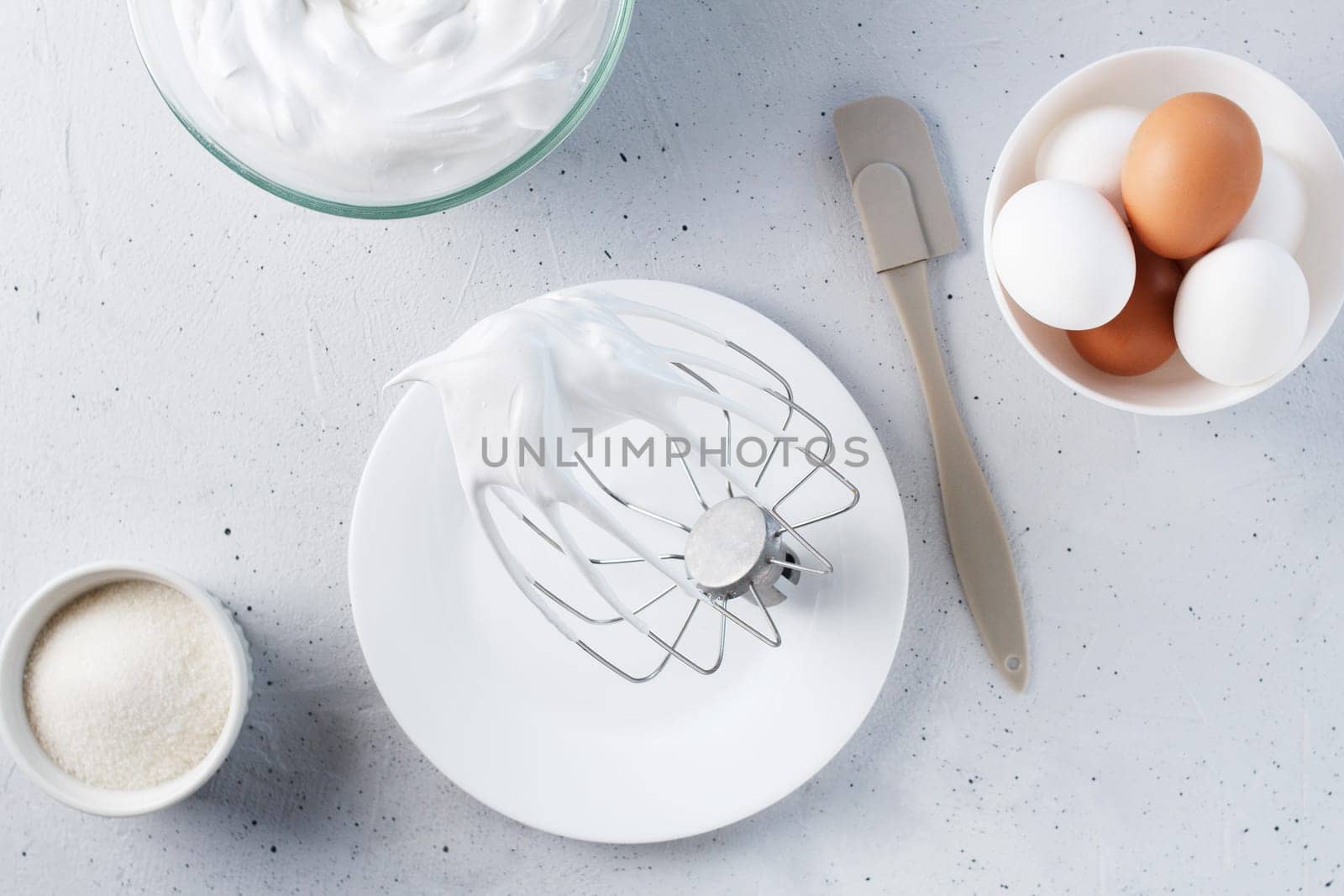 Whipped egg whites - whipped Italian meringue on a wire whisk, eggs, sugar, on a gray background. by lara29