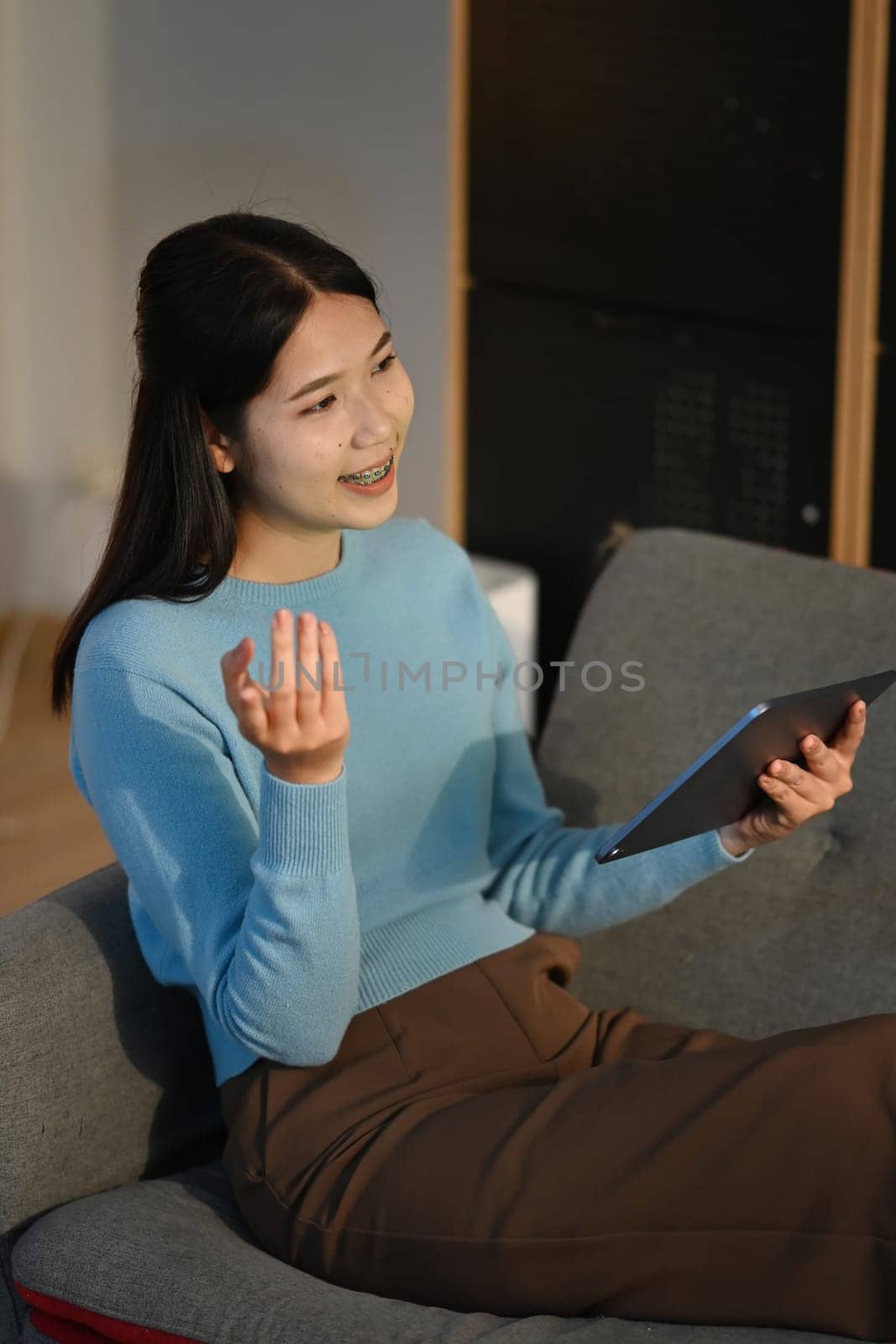 Shot of young woman using her digital tablet while sitting on sofa at home. by prathanchorruangsak