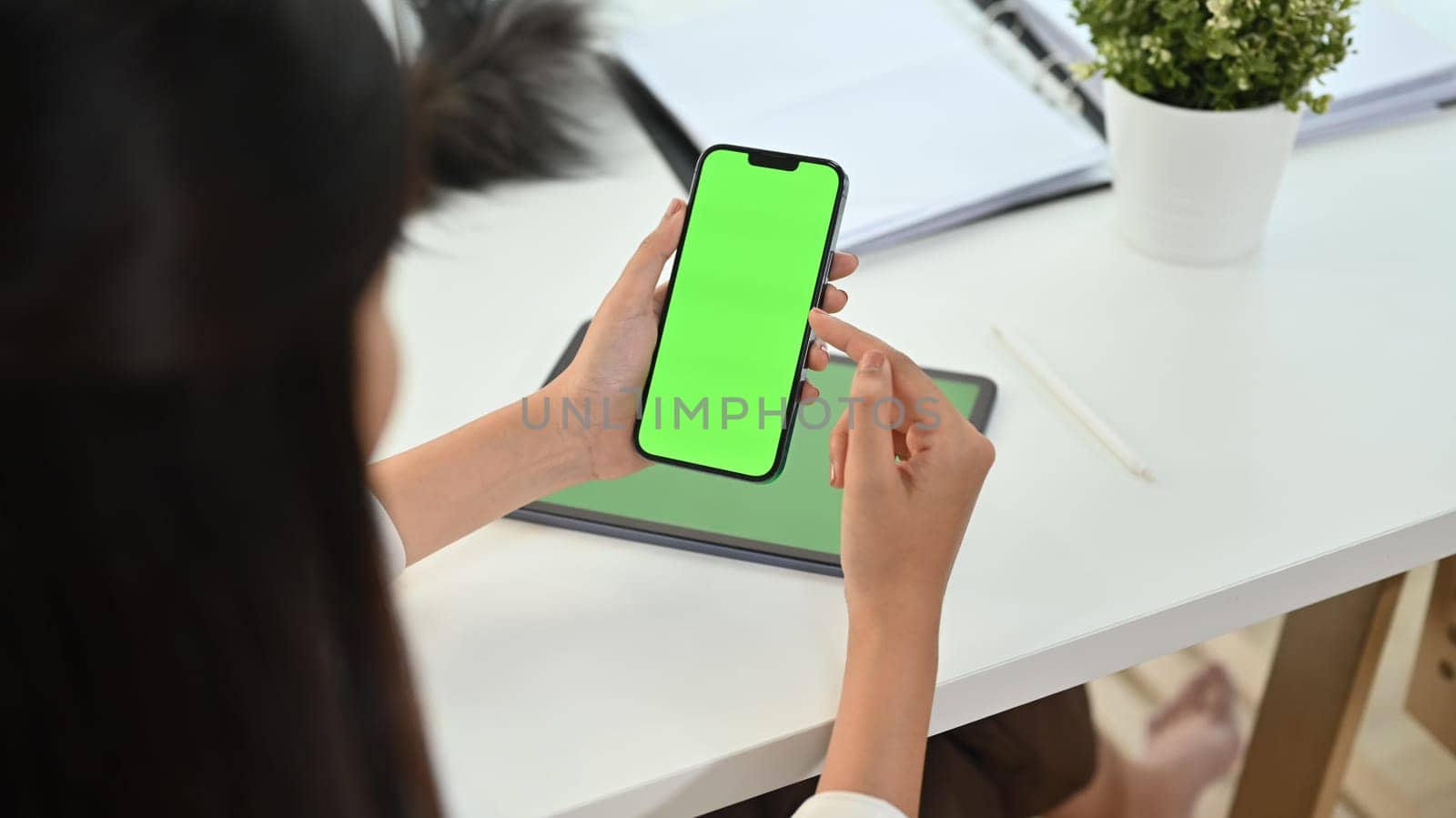 Cropped shot woman holding smartphone with green chrome screen on office desk. by prathanchorruangsak