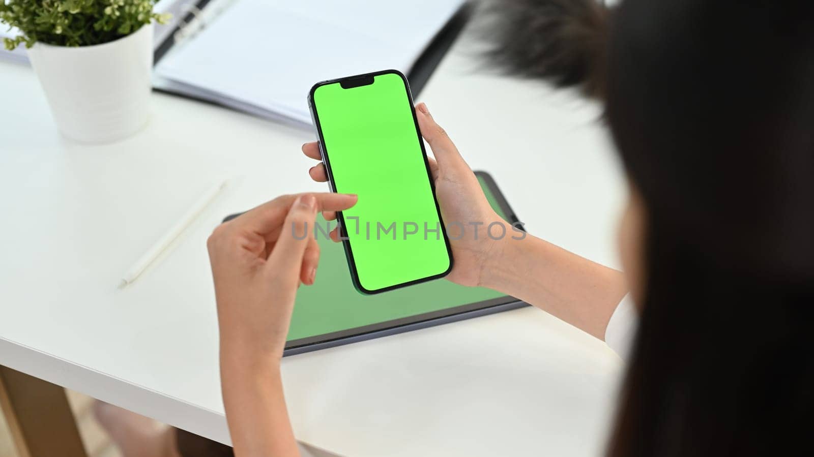 Cropped shot woman holding smartphone with green chrome screen on office desk. High quality photo