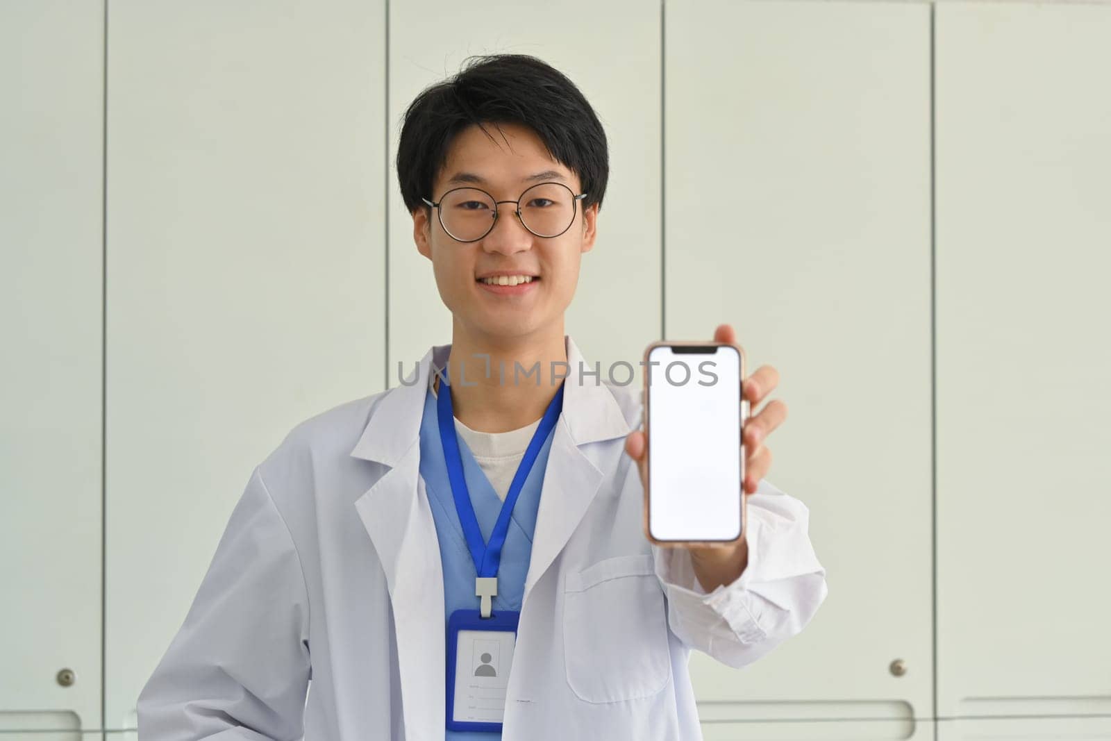 Doctor wearing white uniform showing smartphone with blank screen. Telehealth online applications concept.