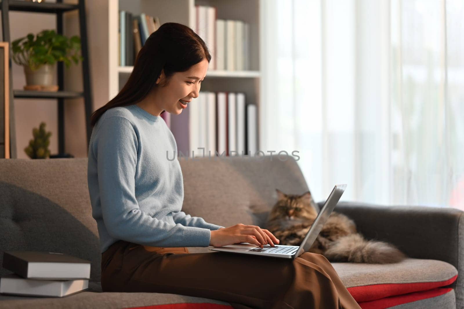 Nice asian woman using laptop computer on couch and smiling moment with domestic cat. by prathanchorruangsak