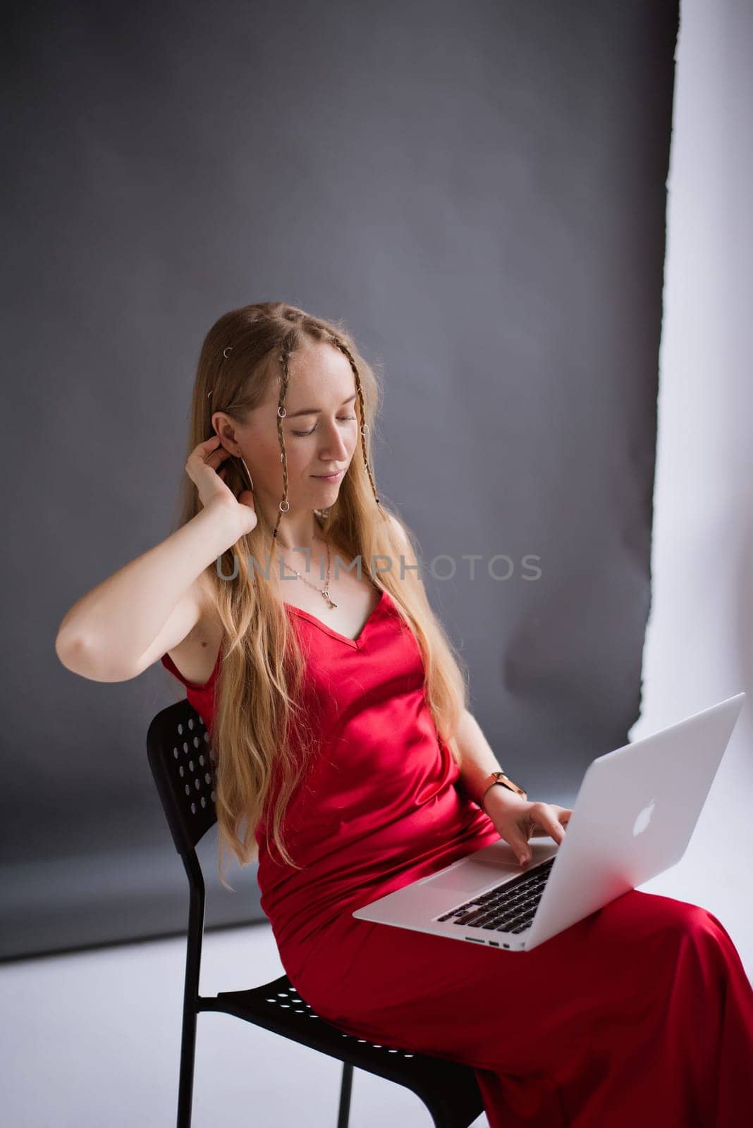 A happy business woman blogger in a red dress is working, typing on a laptop apple and sitting on a chair. portrait blonde assistant of hands with computer MacBook . Vertical