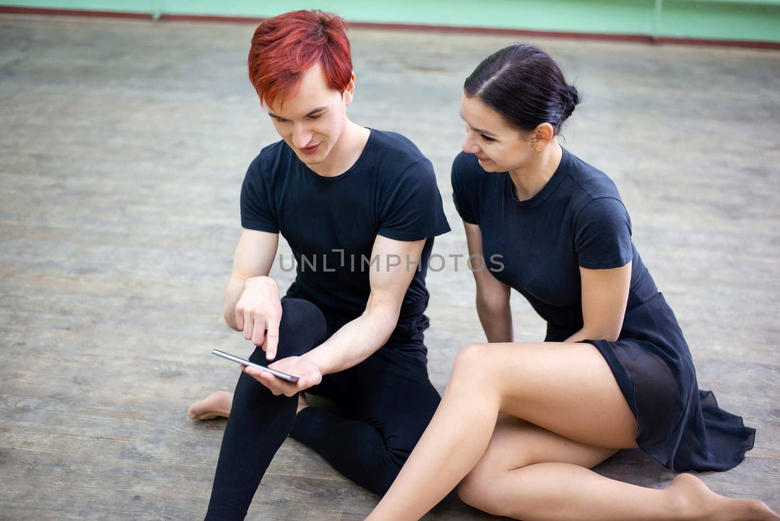 Male and female dancers looking to the mobile phone, learning new performance from video, mastering their skills in choreography